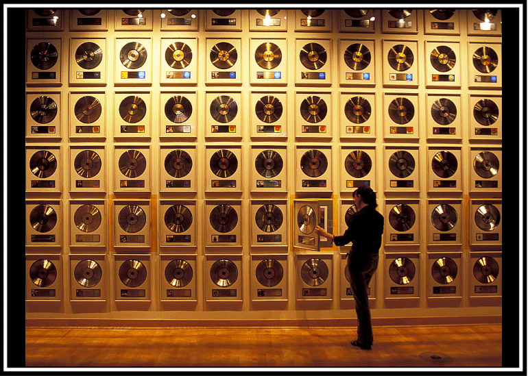 Person observing a wall of awards or plaques in a dimly lit space.