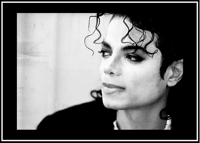 Black and white close-up of Michael Jackson with curly hair and contemplative expression.