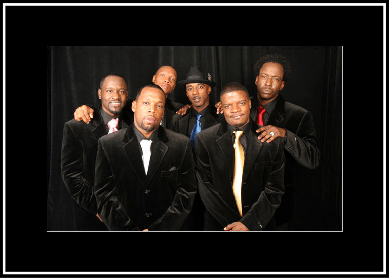 Five men dressed in formal black suits posing together for a photo.